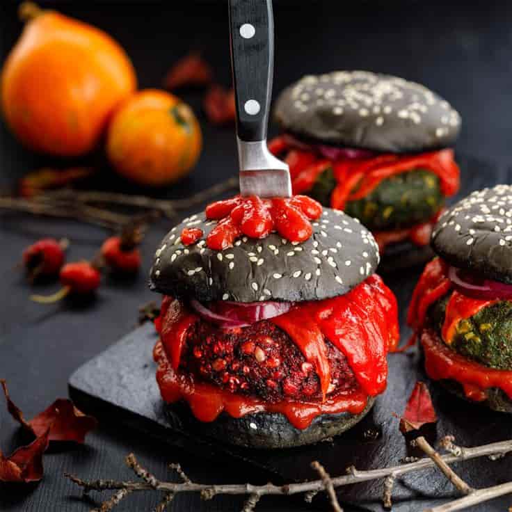 Burger au pain noir avec un couteau planter dedans et plein de ketchup qui dégouline .