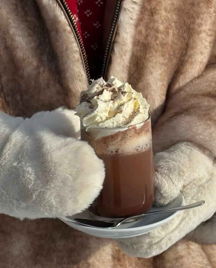 Personne avec un gros manteau et des gants qui tiens un chocolat chaud.