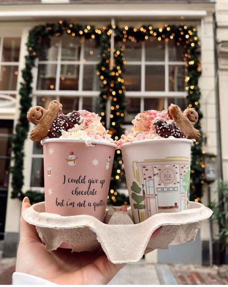 une main qui tien deux boissons devant une fenêtre décorer pour noël.